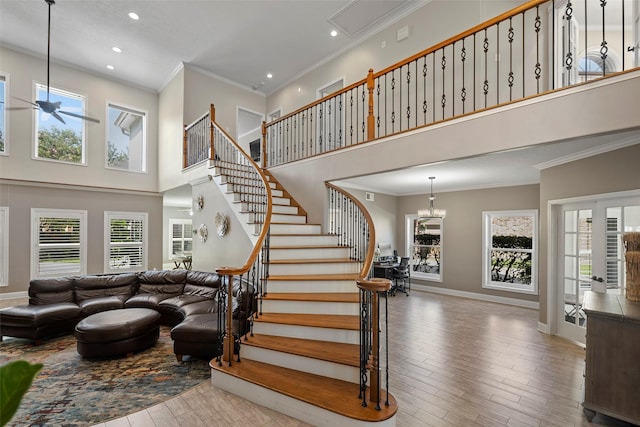 stairs featuring hardwood / wood-style floors, a towering ceiling, a healthy amount of sunlight, and ceiling fan with notable chandelier