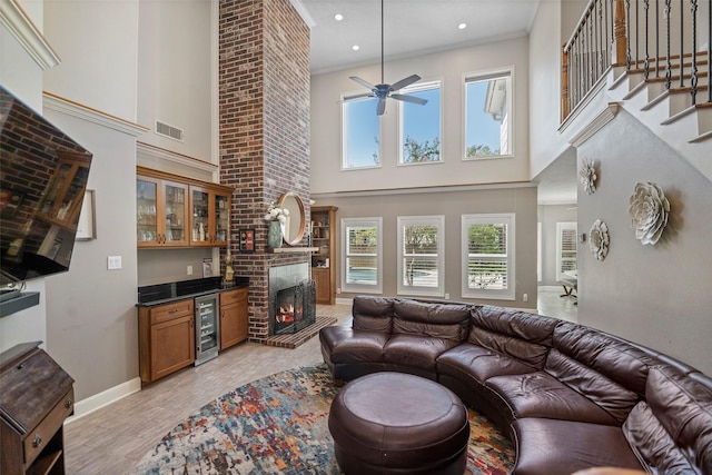 living room with a towering ceiling, a brick fireplace, beverage cooler, indoor bar, and light hardwood / wood-style flooring