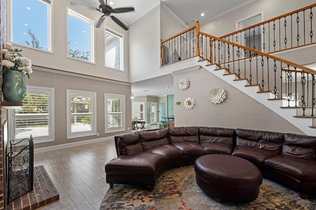 living room featuring hardwood / wood-style floors, ceiling fan, crown molding, and a high ceiling