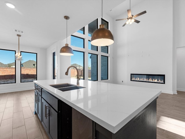 kitchen with plenty of natural light, a kitchen island with sink, sink, and decorative light fixtures