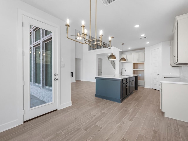 kitchen with sink, pendant lighting, a center island with sink, a notable chandelier, and white cabinets