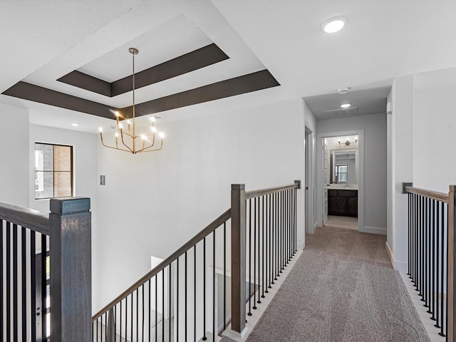 hall with carpet flooring, a tray ceiling, and an inviting chandelier