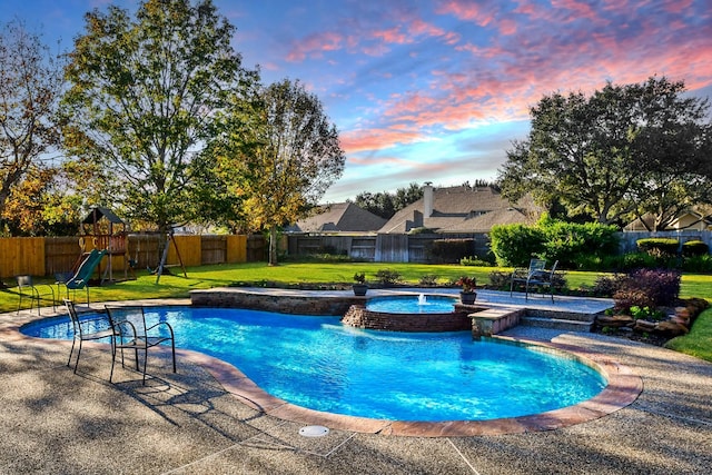 pool at dusk with a playground, a patio area, an in ground hot tub, and a lawn