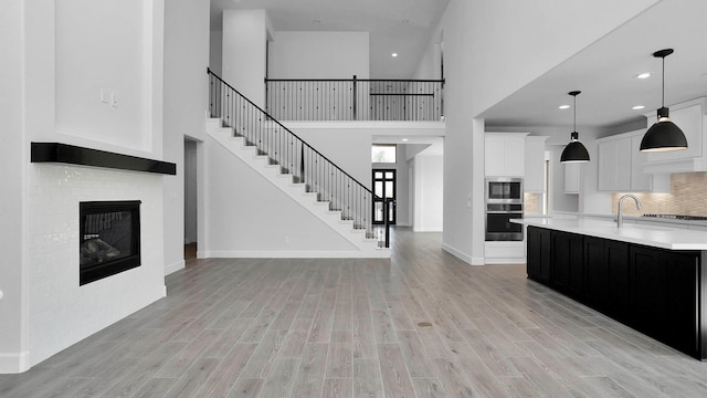 unfurnished living room with a brick fireplace, light wood-type flooring, a towering ceiling, and sink