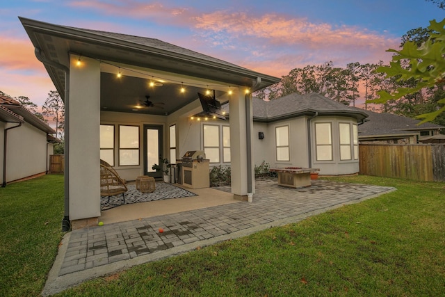 back house at dusk with ceiling fan, a yard, a patio, and exterior kitchen