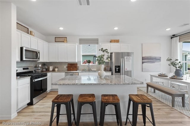 kitchen featuring white cabinets, appliances with stainless steel finishes, light hardwood / wood-style floors, and a center island