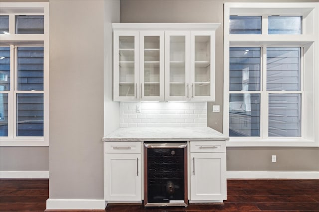 bar with dark wood-type flooring, white cabinetry, light stone countertops, decorative backsplash, and beverage cooler