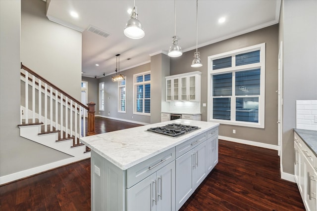 kitchen featuring stainless steel gas stovetop, white cabinetry, decorative backsplash, a kitchen island, and decorative light fixtures