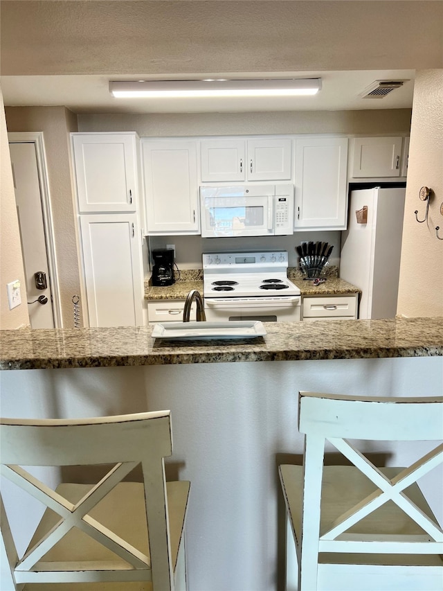 kitchen with white cabinetry, dark stone counters, and white appliances