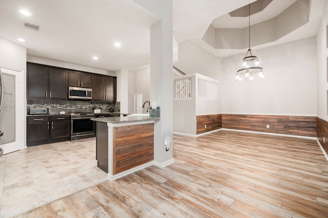 kitchen featuring decorative light fixtures, light stone countertops, stainless steel appliances, and light hardwood / wood-style flooring