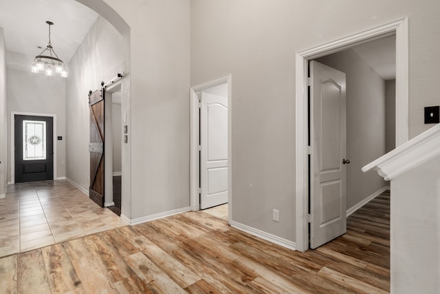 entrance foyer with a barn door, a chandelier, a high ceiling, and light wood-type flooring