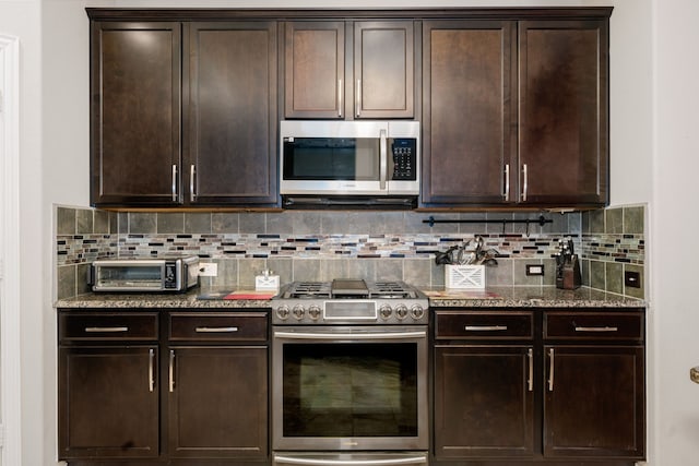 kitchen featuring backsplash, dark brown cabinets, stainless steel appliances, and dark stone counters