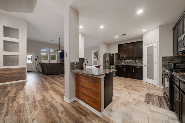 kitchen with kitchen peninsula, appliances with stainless steel finishes, decorative backsplash, dark stone counters, and light hardwood / wood-style flooring