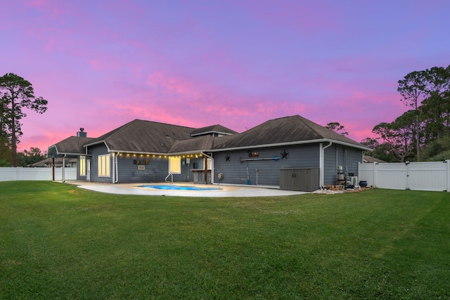 back house at dusk featuring a lawn and a patio area