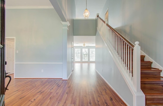 foyer entrance with ceiling fan, a high ceiling, decorative columns, wood-type flooring, and ornamental molding