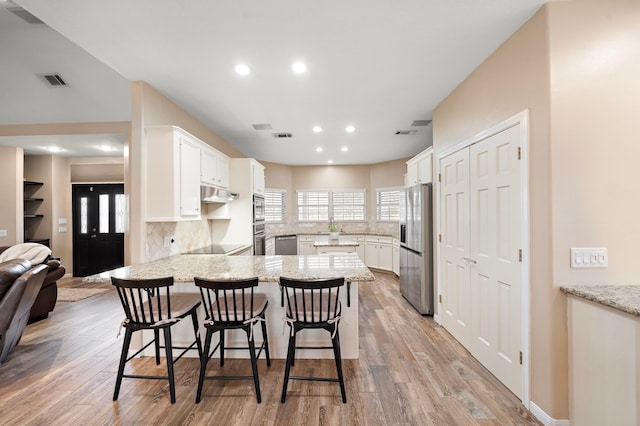 kitchen featuring stainless steel appliances, kitchen peninsula, a kitchen breakfast bar, white cabinets, and light wood-type flooring