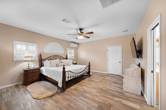 bedroom with a wall mounted AC, light hardwood / wood-style floors, a textured ceiling, and ceiling fan