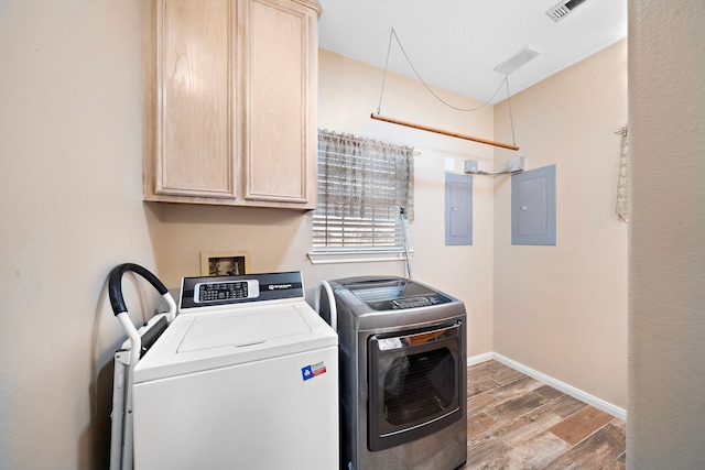 clothes washing area with electric panel, cabinets, hardwood / wood-style floors, and washing machine and dryer