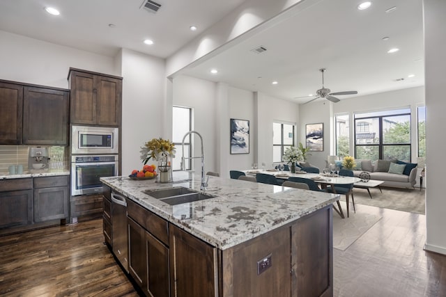 kitchen with stainless steel appliances, dark wood-type flooring, sink, a kitchen island with sink, and light stone countertops