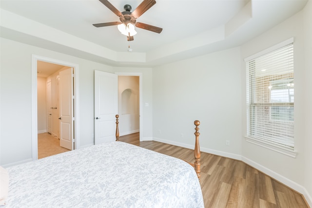 bedroom with light hardwood / wood-style floors, ceiling fan, and a tray ceiling