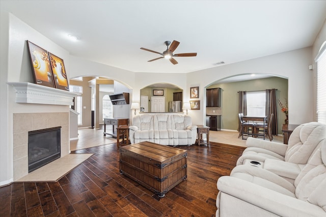 living room featuring dark hardwood / wood-style flooring, ceiling fan, and a tile fireplace