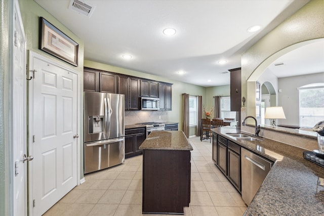 kitchen featuring stainless steel appliances, dark stone counters, sink, a kitchen island, and dark brown cabinets