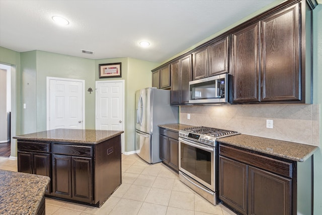 kitchen with dark stone counters, decorative backsplash, dark brown cabinetry, a kitchen island, and appliances with stainless steel finishes