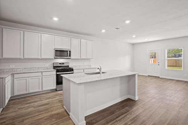 kitchen featuring light stone countertops, white cabinets, appliances with stainless steel finishes, sink, and a center island with sink