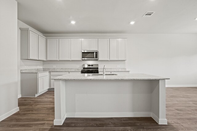 kitchen featuring white cabinets, an island with sink, light stone counters, and appliances with stainless steel finishes