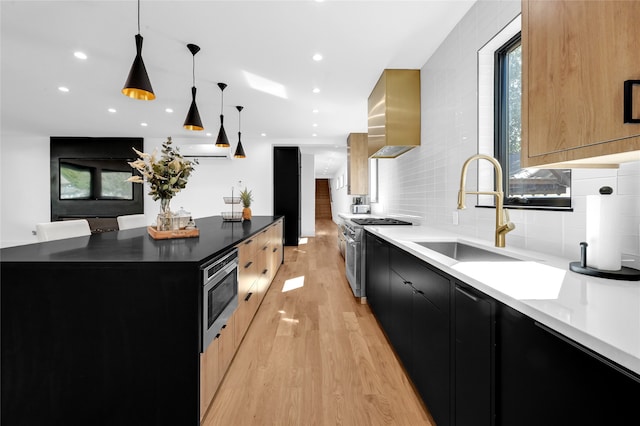 kitchen with stainless steel appliances, wall chimney range hood, a kitchen island, pendant lighting, and light wood-type flooring