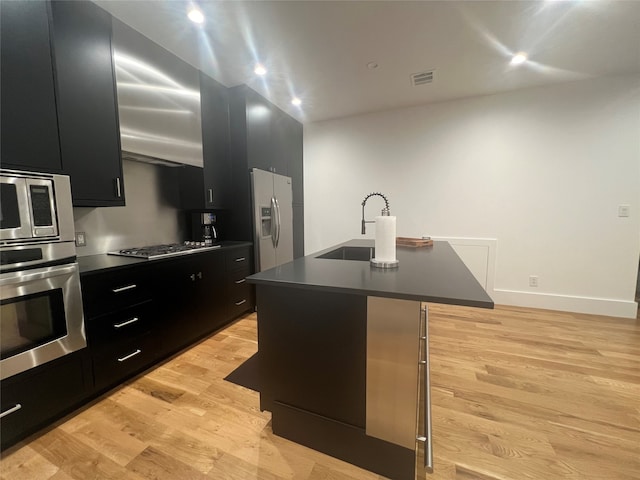 kitchen with stainless steel appliances, sink, an island with sink, a breakfast bar, and light hardwood / wood-style flooring