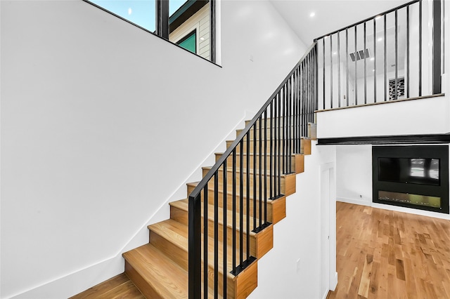 staircase with wood-type flooring and a towering ceiling