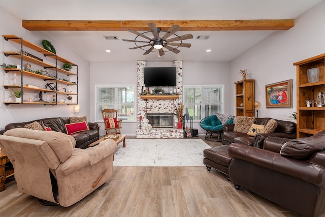 living room featuring ceiling fan, light hardwood / wood-style floors, beamed ceiling, and a stone fireplace