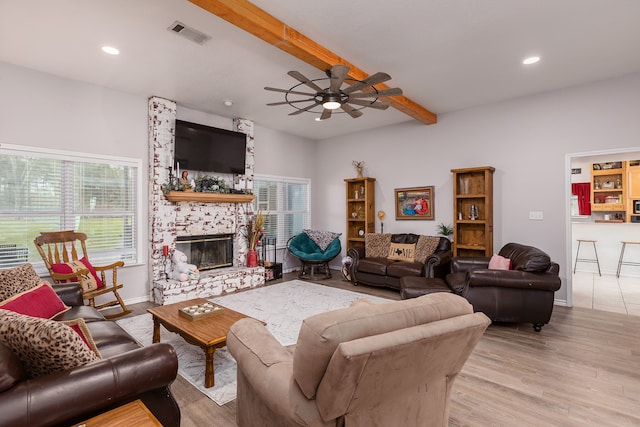 living room featuring a fireplace, ceiling fan, beam ceiling, and light wood-type flooring