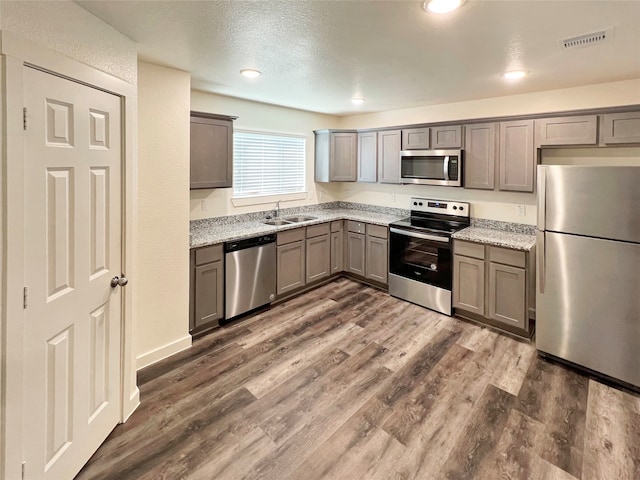 kitchen featuring stainless steel appliances, a textured ceiling, dark hardwood / wood-style flooring, light stone countertops, and sink