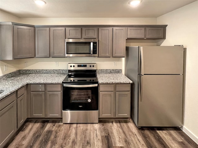 kitchen with gray cabinets, appliances with stainless steel finishes, dark wood-type flooring, and light stone countertops