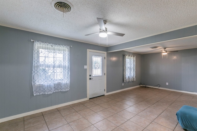 tiled entrance foyer featuring a textured ceiling, wood walls, ceiling fan, and crown molding