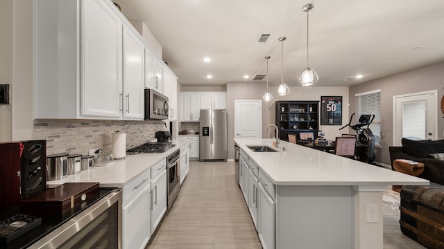 kitchen with stainless steel appliances, white cabinets, hanging light fixtures, sink, and an island with sink