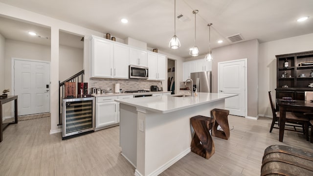 kitchen featuring white cabinetry, appliances with stainless steel finishes, an island with sink, beverage cooler, and pendant lighting