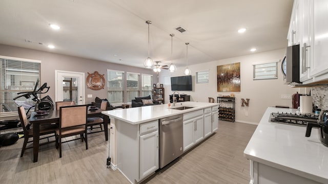 kitchen with a center island with sink, stainless steel appliances, white cabinetry, pendant lighting, and sink