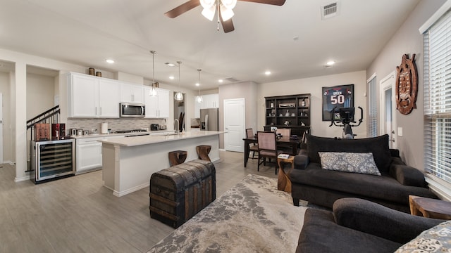 living room with beverage cooler, sink, ceiling fan, and light hardwood / wood-style flooring