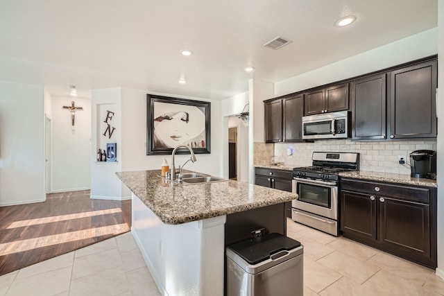 kitchen featuring light stone counters, appliances with stainless steel finishes, sink, an island with sink, and light hardwood / wood-style floors