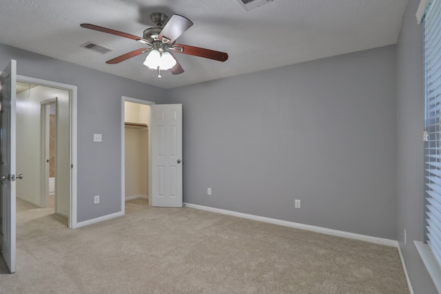 unfurnished bedroom with a textured ceiling, light carpet, ceiling fan, a closet, and a spacious closet