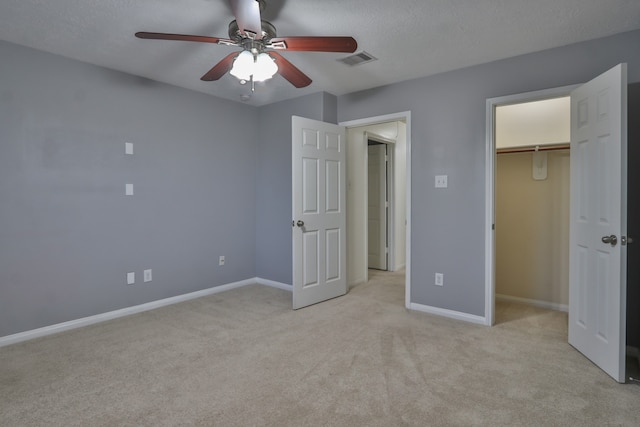 unfurnished bedroom with a closet, a spacious closet, a textured ceiling, light colored carpet, and ceiling fan