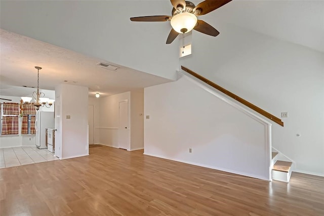 unfurnished living room featuring ceiling fan with notable chandelier and light hardwood / wood-style flooring