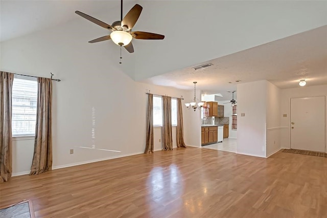 unfurnished living room with light wood-type flooring, ceiling fan with notable chandelier, and high vaulted ceiling