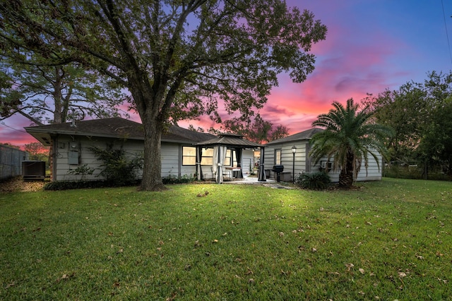 back house at dusk with a gazebo, central air condition unit, and a lawn