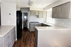 kitchen with sink, black fridge, kitchen peninsula, dark hardwood / wood-style floors, and backsplash