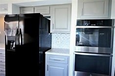 kitchen with stainless steel double oven, black fridge, tasteful backsplash, and white cabinetry