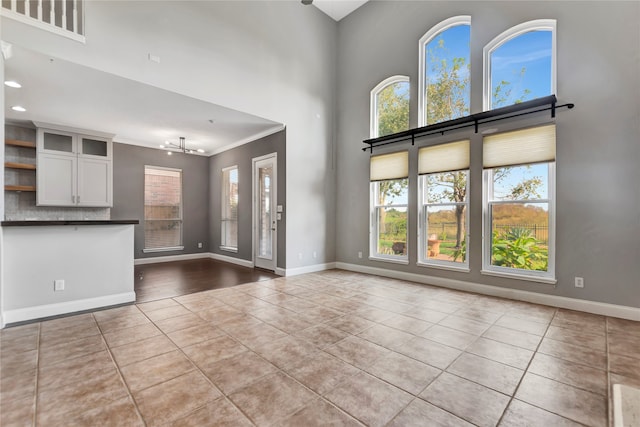 unfurnished living room featuring crown molding, light tile patterned floors, a high ceiling, and an inviting chandelier